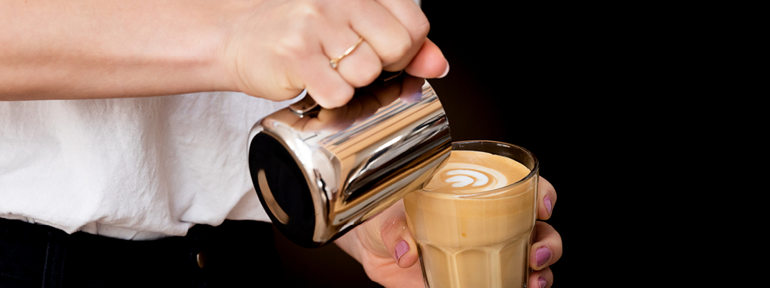 VISUELL Blogbeitrag: Kaffeegenuss: In ein Glas voll Kaffee wird Milch als Latte-Art gegossen